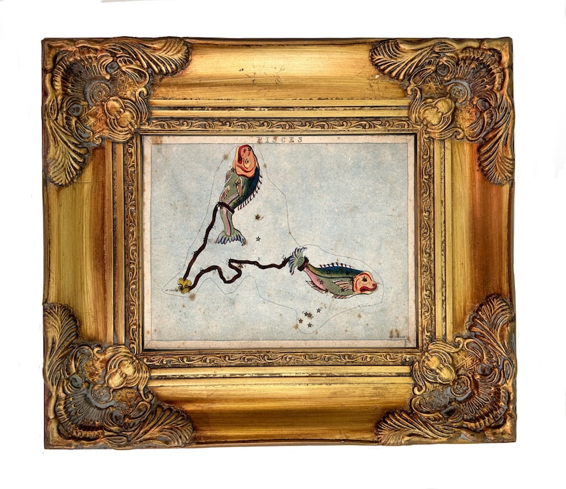 May include: A framed illustration of the Pisces constellation featuring two stylized fish connected by a dark line on a light blue background. The word PISCES is printed at the top. The frame is ornate, metallic gold with decorative corner details.
