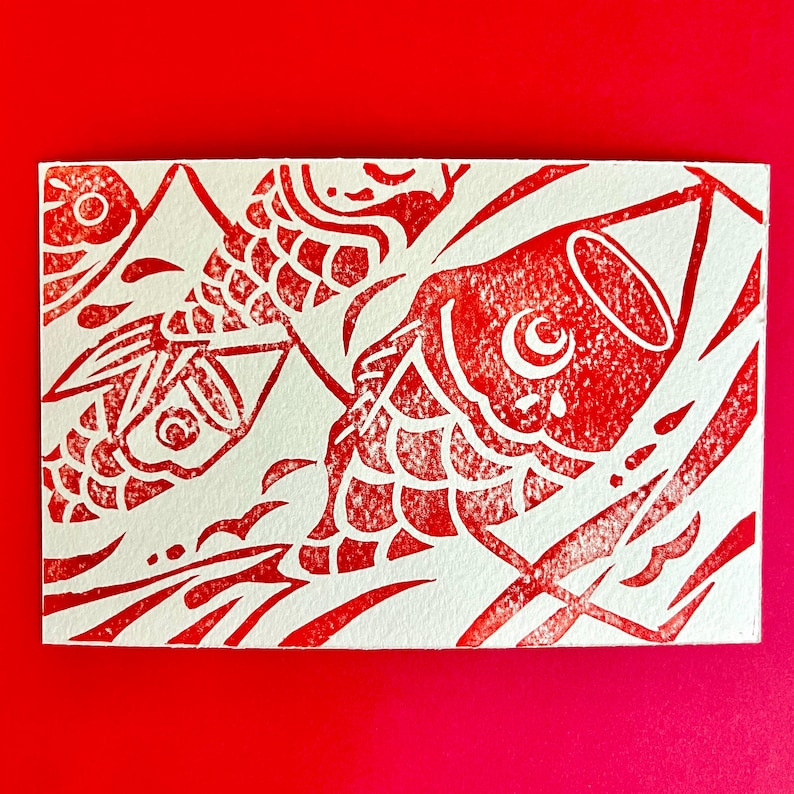 May include: A red and white print featuring stylized koi fish. The design is a linocut style, with the fish and water details in red against a white background. The artwork is on a rectangular card.