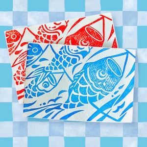 May include: Two rectangular cards with carp designs. One card features a red carp print, and the other has a blue carp print. The carp are stylized with detailed scales and fins. The background is a light blue and white checkered pattern.