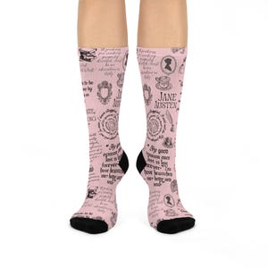 May include: Pink knee-high socks with a black heel and toe. The socks are covered in a repeating pattern of Jane Austen quotes, illustrations, and the author's name in black.