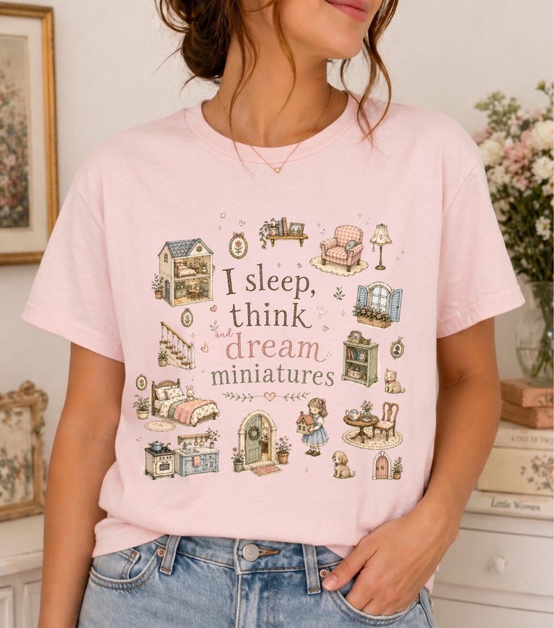 May include: A light pink t-shirt featuring a whimsical illustration of miniature dollhouse furniture and the text "I sleep, think and dream miniatures". The design includes a bed, armchair, and a dollhouse.