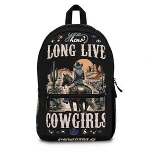 May include: A black backpack featuring a graphic print of a person riding a horse in a desert landscape with cacti and rock formations. The text "yee haw" appears at the top, with "LONG LIVE" above the scene and "COWGIRLS" printed below.