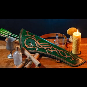 May include: A green leather quiver with gold accents and intricate carvings. The quiver is filled with arrows and is resting on a wooden table with a candle and other items.