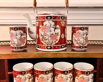 May include: A red and white porcelain teapot with a bamboo handle and floral design. The teapot is surrounded by six matching teacups with floral designs.