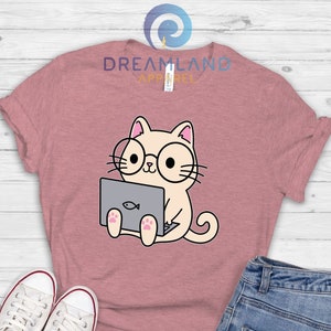 May include: A heather mauve t-shirt with the text "Dreamland Apparel" printed on the front. The shirt features a cartoon illustration of a cat wearing glasses and using a laptop.