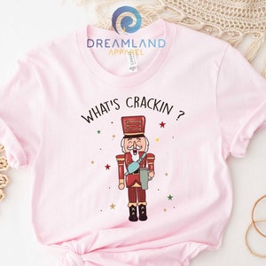 May include: Pink t-shirt with a graphic of a nutcracker and the text "What's Crackin?"