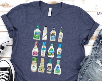 May include: A heather navy blue t-shirt with a graphic of various salad dressing bottles. The text "Dreamland Apparel" is printed on the top right corner of the shirt.