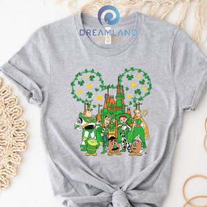 May include: A gray t-shirt with a green shamrock design featuring characters from the Toy Story franchise in front of a green castle. The text "DREAMLAND APPAREL" is on the shirt.