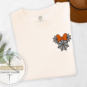 Pu&ograve; includere: T-shirt color crema con un ricamo a tema Halloween. Il design presenta una ragnatela nera con un fiocco arancione. La maglietta &egrave; di Comfort Colors ed &egrave; un regalo personalizzato.