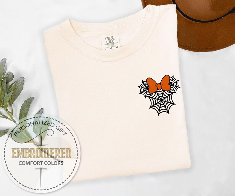 Pu&ograve; includere: T-shirt color crema con un ricamo a tema Halloween. Il design presenta una ragnatela nera con un fiocco arancione. La maglietta &egrave; di Comfort Colors ed &egrave; un regalo personalizzato.