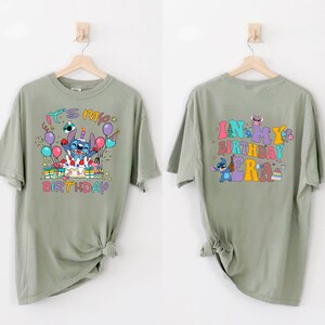Puede incluir: Una camiseta verde con un personaje azul Stitch en la parte delantera. La camiseta dice "It's my birthday" en letras de colores. La parte posterior de la camiseta dice "In my birthday era" en letras de colores con un personaje Stitch en la parte posterior.