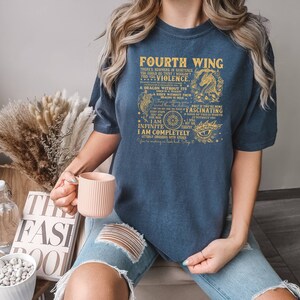 May include: A navy blue t-shirt with a gold graphic print that reads "Fourth Wing" and includes a dragon, a compass, and an eye. The text on the shirt reads "There's nowhere in existence you could go that I wouldn't find you...Violence. A dragon without its dragon is dear. Only if you're mine I am infinite. I am completely utterly obsessed with you. You're making me lose it. Stay it."
