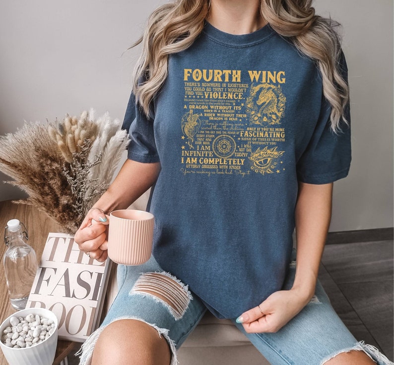 May include: A navy blue t-shirt with a gold graphic print that reads "Fourth Wing" and includes a dragon, a compass, and an eye. The text on the shirt reads "There's nowhere in existence you could go that I wouldn't find you...Violence. A dragon without its dragon is dear. Only if you're mine I am infinite. I am completely utterly obsessed with you. You're making me lose it. Stay it."