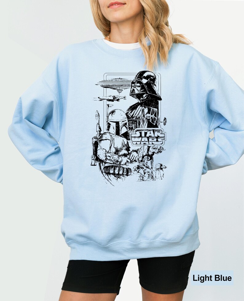 May include: Light blue sweatshirt featuring a black and white Star Wars graphic. The graphic includes Darth Vader, Boba Fett, and the Star Wars logo. The sweatshirt has long sleeves and a crew neck.