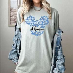 Puede incluir: Una camiseta azul claro con un dise&ntilde;o de Mickey Mouse floral azul y la palabra "Ohana" en letras negras.