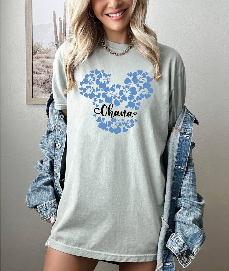 Puede incluir: Una camiseta azul claro con un dise&ntilde;o de Mickey Mouse floral azul y la palabra "Ohana" en letras negras.