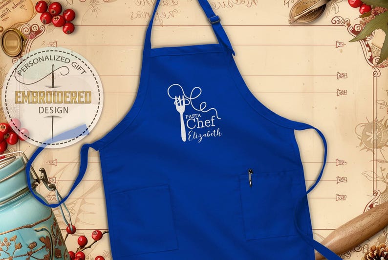 May include: A royal blue apron with a white embroidered design featuring a fork and spaghetti, with the words "Pasta Chef Elizabeth". The apron has two front pockets and an adjustable neck strap. The apron is a personalized gift.