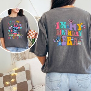 Puede incluir: Una camiseta gris con un personaje de dibujos animados azul que sostiene una guitarra y el texto "In My Birthday Era". La parte delantera de la camiseta tiene una versi&oacute;n m&aacute;s peque&ntilde;a del personaje con el texto "It's My Birthday".