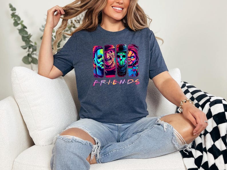 May include: Dark blue t-shirt featuring a colorful graphic of four horror movie characters. The word "FRIENDS" is printed in a rainbow font below the characters. The shirt is made of a soft material.