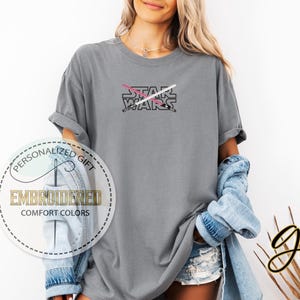 Może przedstawiać: Szara koszulka z nadrukiem "STAR WARS" i wzorem r&oacute;żowego i białego miecza świetlnego.