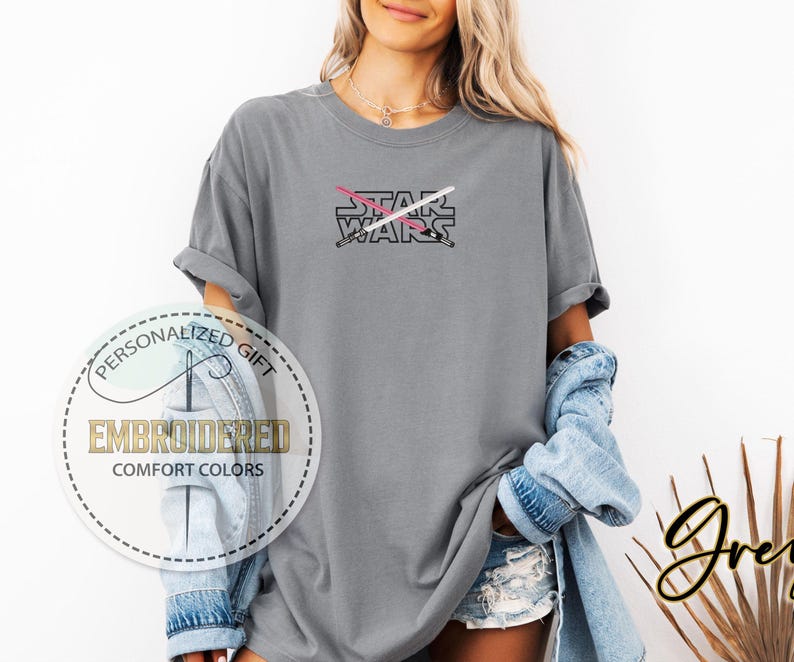 Może przedstawiać: Szara koszulka z nadrukiem "STAR WARS" i wzorem r&oacute;żowego i białego miecza świetlnego.