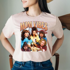 Puede incluir: Una camiseta rosa con un estampado gr&aacute;fico de un grupo de mujeres con el texto "Mom Vibes Cool Moms Club".