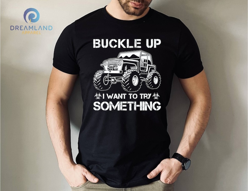 Op de afbeelding: Zwart T-shirt met een witte afbeelding van een jeep met de tekst "Buckle Up I Want To Try Something"