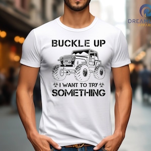Op de afbeelding: Wit T-shirt met een zwarte afbeelding van een jeep en de tekst "Buckle Up I Want To Try Something".