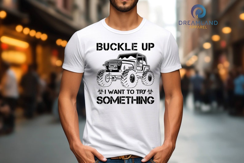 Op de afbeelding: Wit T-shirt met een zwarte afbeelding van een jeep en de tekst "Buckle Up I Want To Try Something".