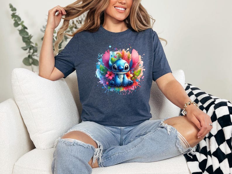 Op de afbeelding: Marineblauw t-shirt met een kleurrijke afbeelding van een blauw stripfiguur omringd door bloemen en verfspatten. Het ontwerp is gecentreerd op het shirt, wat zorgt voor een levendige en speelse uitstraling. Het shirt is gemaakt van zacht materiaal.