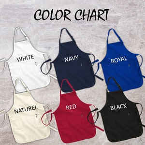 May include: A color chart displaying six aprons in various colors: white, navy, royal blue, natural, red, and black. Each apron has a pocket and the color name printed on it. The aprons are displayed against a marble background.