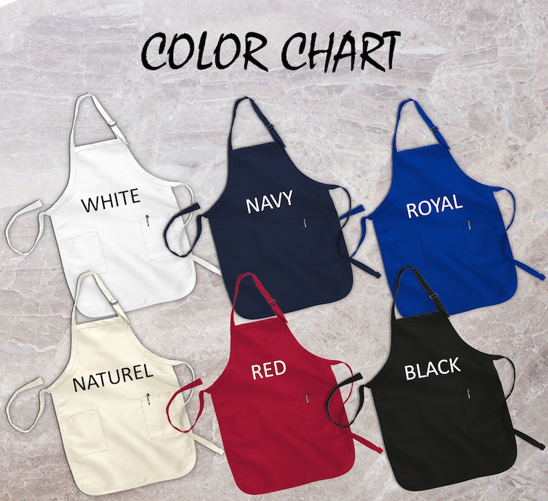 May include: A color chart displaying six aprons in various colors: white, navy, royal blue, natural, red, and black. Each apron has a pocket and the color name printed on it. The aprons are displayed against a marble background.
