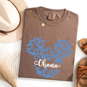 Puede incluir: Camiseta marr&oacute;n con un dise&ntilde;o de Mickey Mouse floral azul y la palabra "Ohana" impresa en blanco.
