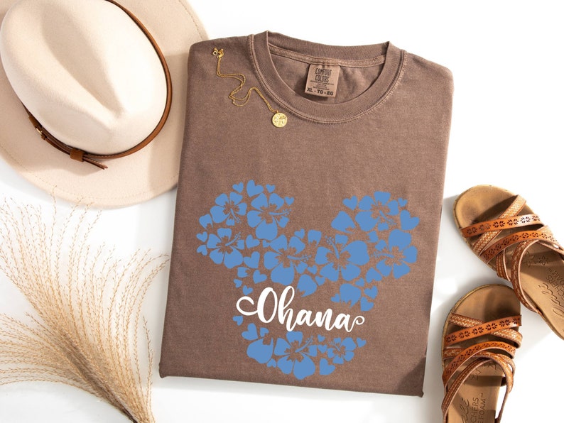 Puede incluir: Camiseta marr&oacute;n con un dise&ntilde;o de Mickey Mouse floral azul y la palabra "Ohana" impresa en blanco.