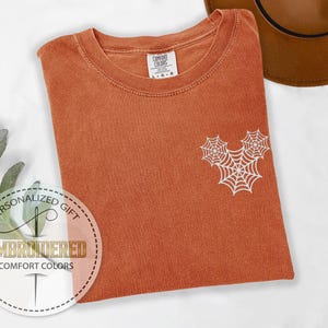 Pu&ograve; includere: T-shirt Comfort Colors arancione bruciato con un disegno a ragnatela bianca. La maglietta ha girocollo e maniche corte. L'etichetta recita "Comfort Colors". La maglietta &egrave; piegata e ha un adesivo rotondo con la scritta "Regalo personalizzato" e "Embroidered Comfort Colors".