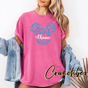 Puede incluir: Camiseta rosa con un dise&ntilde;o de Mickey Mouse floral azul y la palabra "Ohana" en letras blancas.