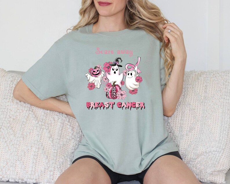 Pode incluir: Uma camiseta verde claro com uma fita rosa, fantasmas e uma ab&oacute;bora com o texto "Scare away Breast Cancer".