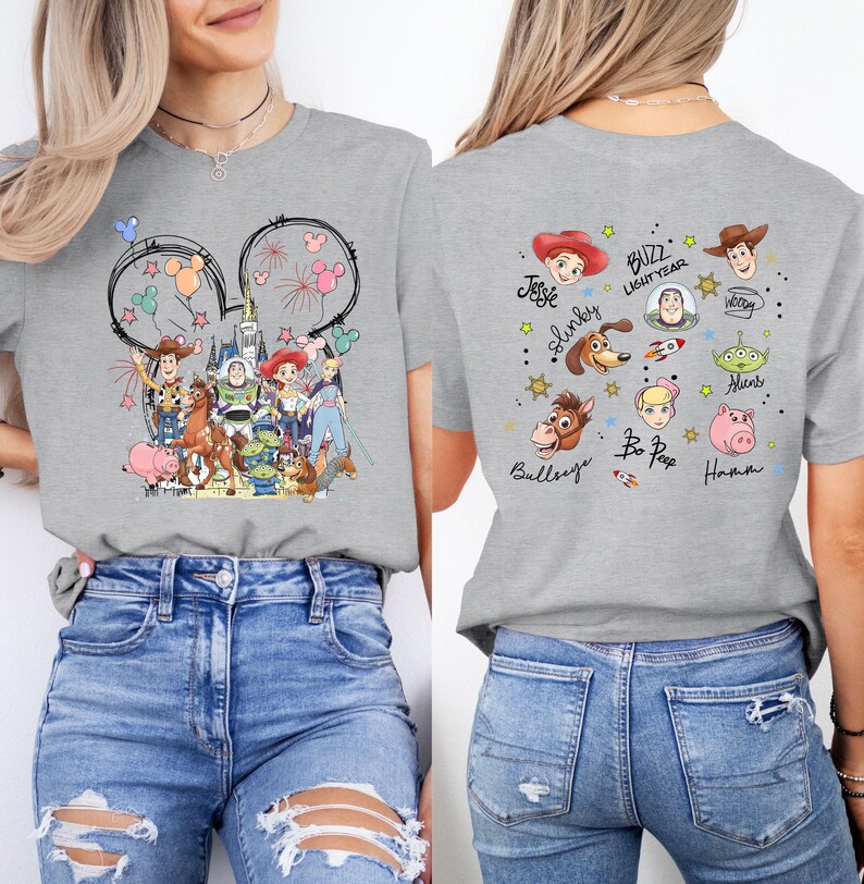 May include: A grey t-shirt with a Disney theme. The front has Mickey Mouse ears with fireworks and Disney characters. The back of the shirt features various Toy Story characters and their names.