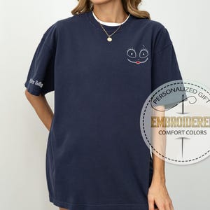 K&ouml;nnte beinhalten: Marineblaues, besticktes Comfort Colors T-Shirt mit einem Cartoon-Gesicht auf der Vorderseite und "His Sally" auf dem &Auml;rmel. Das Design hat einen wei&szlig;en Umriss mit schwarzen Augen und einem roten Mund. Das Shirt ist ein personalisiertes Geschenk.