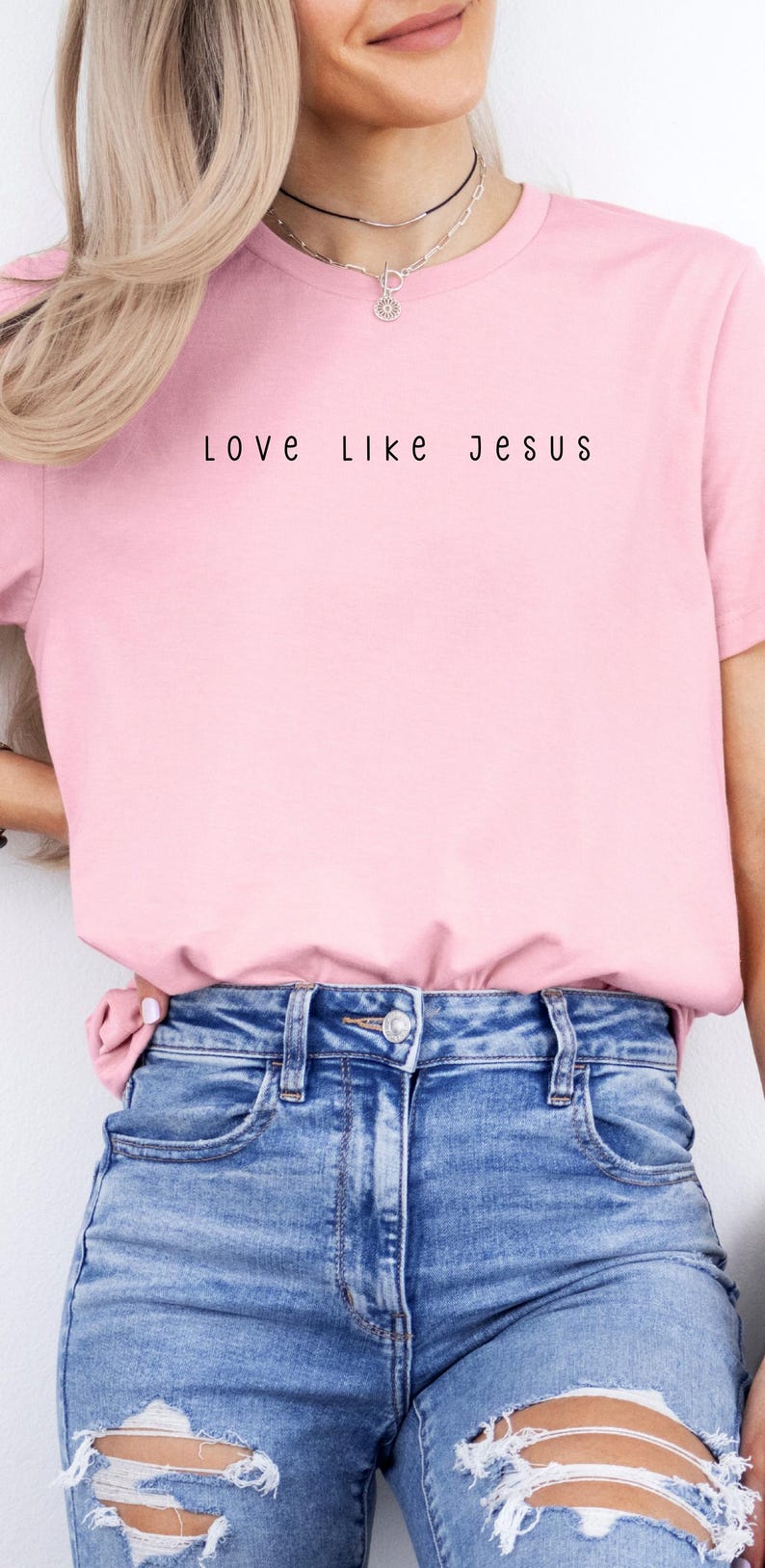 May include: A light pink t-shirt with the text "Love Like Jesus" in black lettering. The shirt is paired with blue denim jeans. The overall style is casual and comfortable.