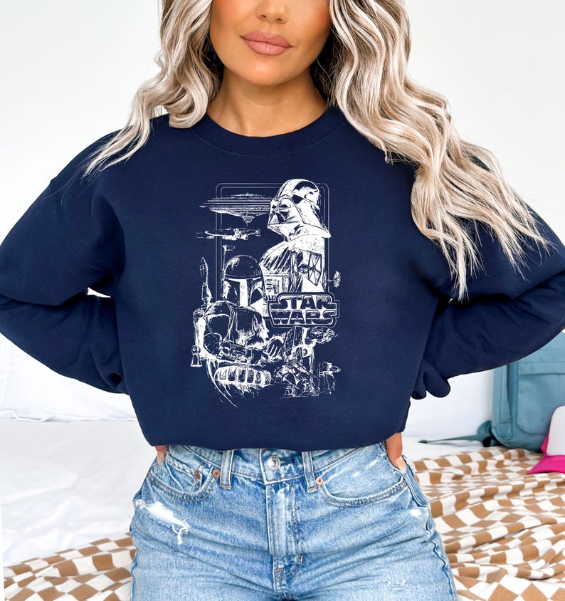 May include: Navy blue sweatshirt featuring a white graphic of Star Wars characters and elements, including Darth Vader, Boba Fett, and the Star Wars logo. The design is a detailed illustration of the iconic characters and spacecraft from the film series.