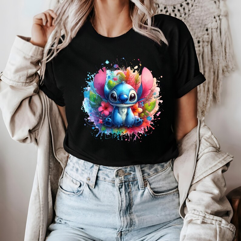 Op de afbeelding: Zwart t-shirt met een kleurrijk aquarelontwerp van Stitch uit Lilo & Stitch. Het kunstwerk toont het personage met roze oren, blauwe vacht en bloemaccenten, omringd door verfspatten.