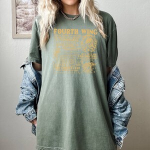 May include: A green oversized t-shirt with a vintage-style graphic design that reads "Fourth Wing" and includes a detailed illustration of a dragon. The text is in a gold color.