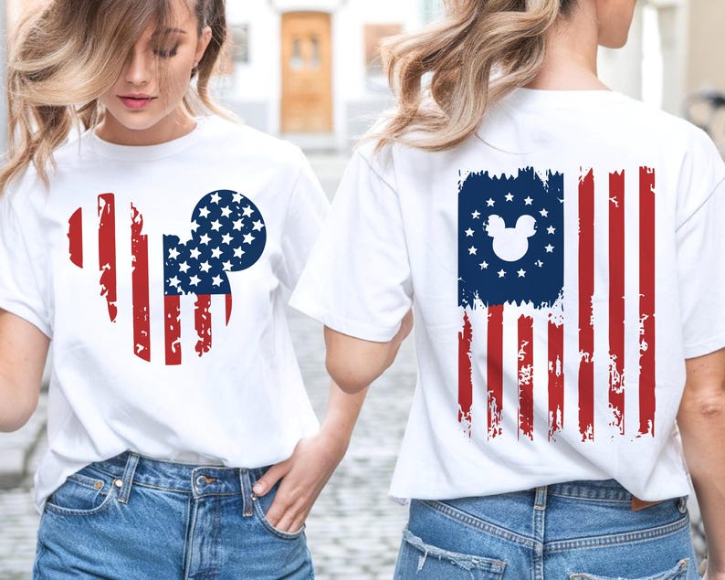 May include: White t-shirts with a distressed American flag design featuring a Mickey Mouse silhouette. The front design is a Mickey Mouse head with red stripes and a blue circle filled with white stars. The back design is a distressed American flag with a Mickey Mouse head in the blue field.