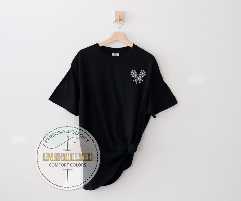 Pu&ograve; includere: T-shirt nero con un disegno a ragnatela ricamata bianca sulla parte superiore sinistra del petto. La maglietta &egrave; del marchio Comfort Colors. L'immagine include anche un logo circolare con le parole "Personalized Gift" e "Embroidered Comfort Colors".