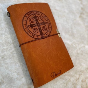 May include: A brown leather journal with a Saint Christopher medal design and the name "David" embossed on the front.