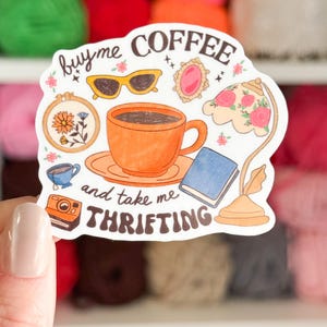 Może przedstawiać: Naklejka z napisem "buy me coffee and take me thrifting" z ilustracjami filiżanki kawy, okular&oacute;w przeciwsłonecznych, aparatu fotograficznego, książki i lampy. Naklejka ma białe tło i r&oacute;żnorodne kolorowe ilustracje.