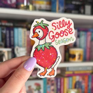 Op de afbeelding: Een sticker met een cartoon-gans die een aardbeikostuum draagt. De sticker heeft een holografische afwerking en zegt "Silly Goose Season".