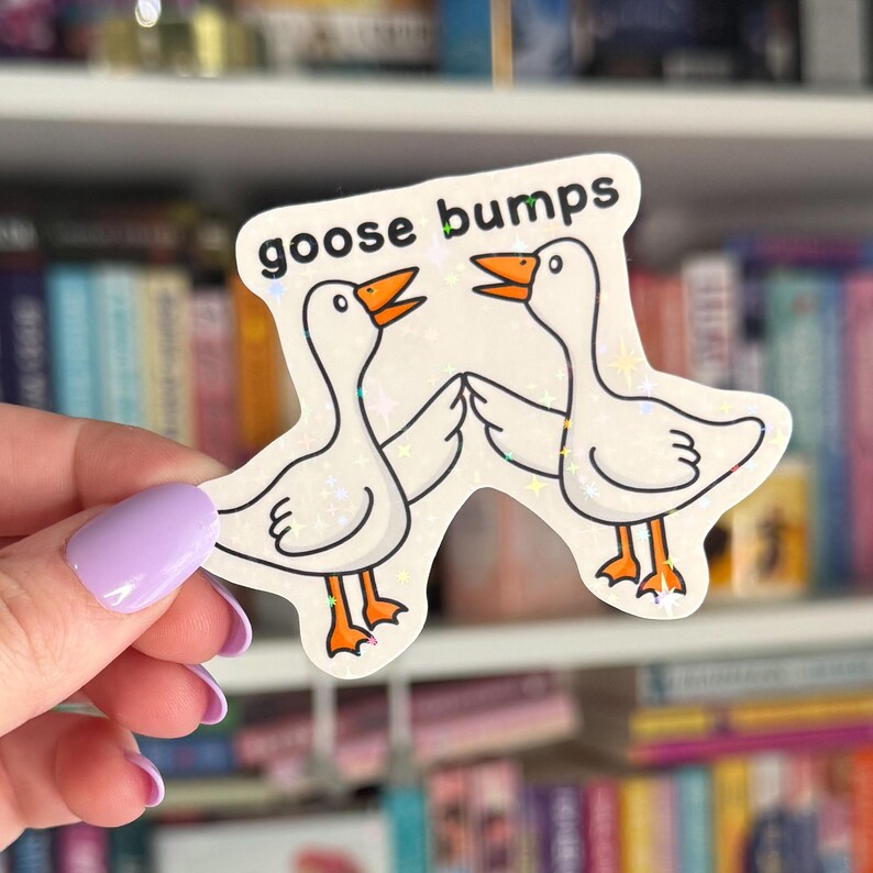 Op de afbeelding: Een witte sticker met twee cartoon-ganzen die elkaar aankijken. De ganzen zijn wit met oranje snavels en poten. De tekst "goose bumps" is in het zwart bovenaan de sticker gedrukt.