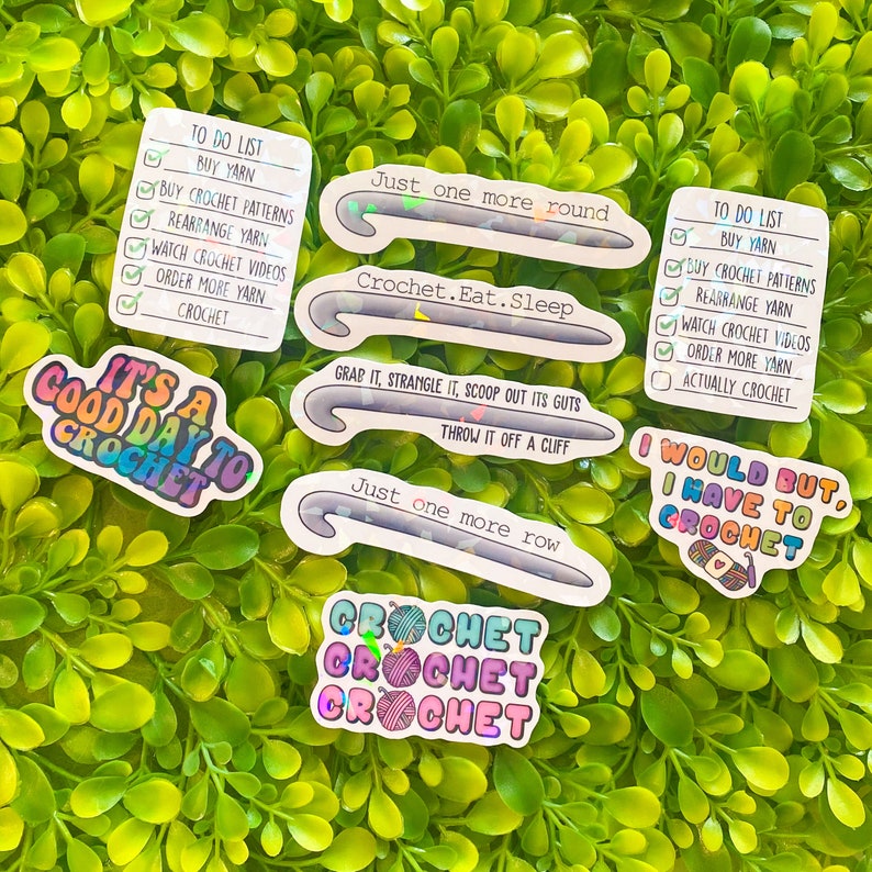 May include: A collection of colorful crochet-themed stickers with various phrases and a to-do list. The stickers feature crochet hooks and text like "Just one more round" and "It's a good day to crochet."